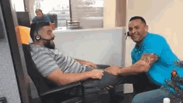 a man wearing a headset is sitting in a chair while another man holds his leg .