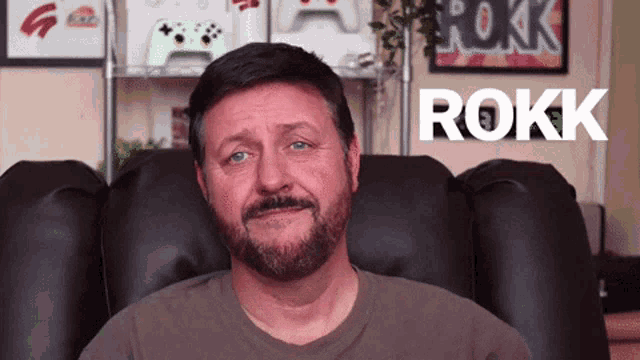 a man with a beard is sitting in a chair with rokk written in white letters behind him