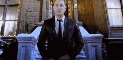 a man in a suit and tie is standing with his hands in his pockets .