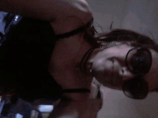 a woman wearing sunglasses and a choker looks down at something