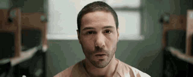 a man with a beard is looking at the camera in a room with a window .