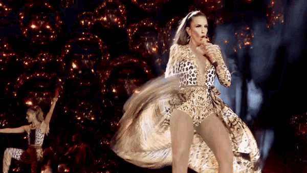 a woman in a leopard print dress is singing into a microphone on a stage