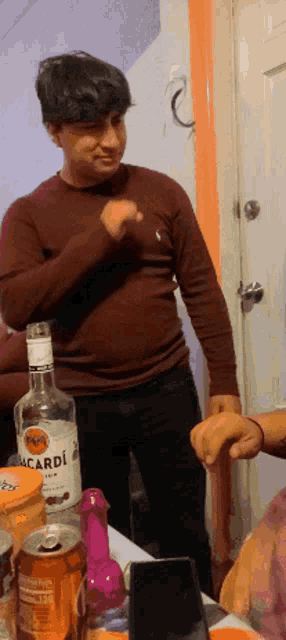 a man in a brown shirt is standing next to a bottle of bacardi