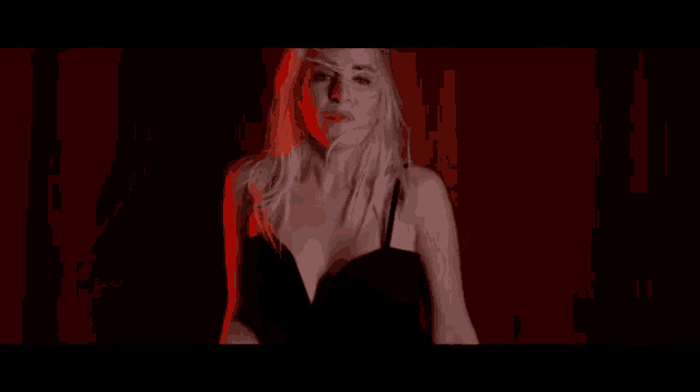 a blonde woman in a black dress is singing in front of a red curtain .