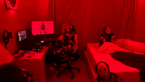 a woman sits in a chair in front of a computer monitor in a room with red lighting