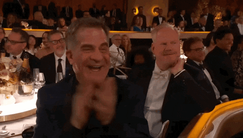 a man in a tuxedo is laughing while sitting at a table