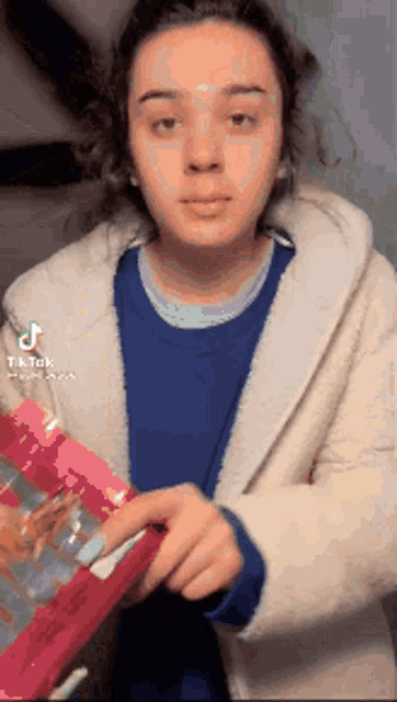 a woman in a blue sweater and white coat is holding a pink bag in her hand .