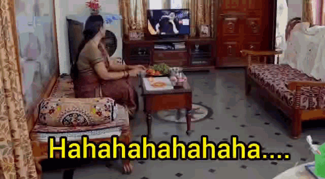 a woman is sitting on a couch in a living room laughing while watching television .