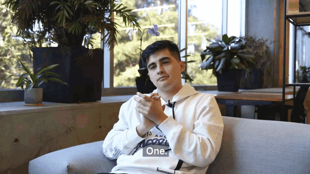 a man sitting on a couch with the word one on his sweatshirt
