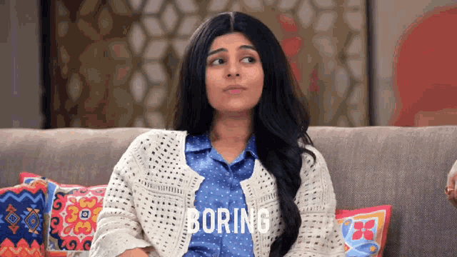 a woman is sitting on a couch and the word boring is on the screen behind her
