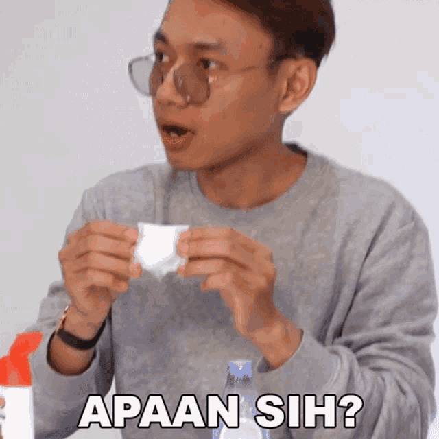 a man wearing glasses is holding a piece of paper with the words apaan sih written on it