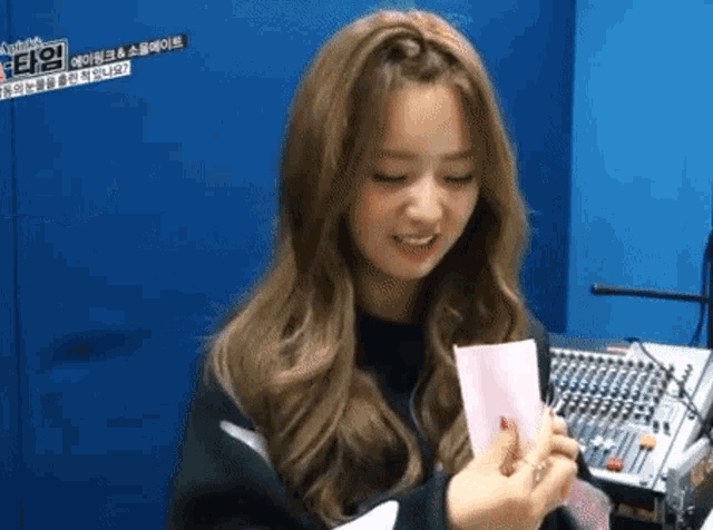a girl is holding a piece of paper in front of a blue wall and a microphone .