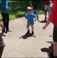 a group of people are standing on a sidewalk with a little boy in a blue shirt standing in the middle .