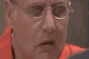 a bald man in a red shirt is covering his face with his hands .