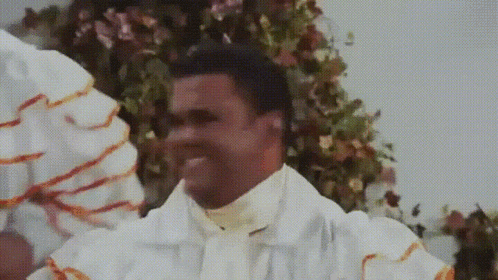 a man in a white robe is smiling in front of a flower arrangement