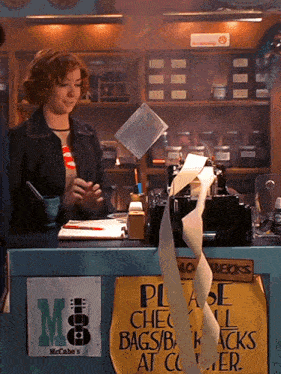 a woman standing behind a counter with a sign that says please check bags / bags at counter