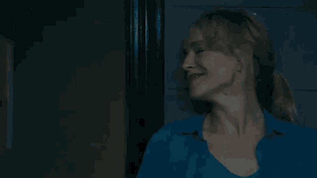 a woman in a blue shirt is smiling and looking at the camera .