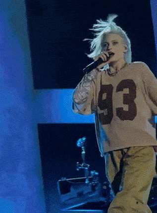 a woman is singing into a microphone wearing a sweater with the number 93 on it