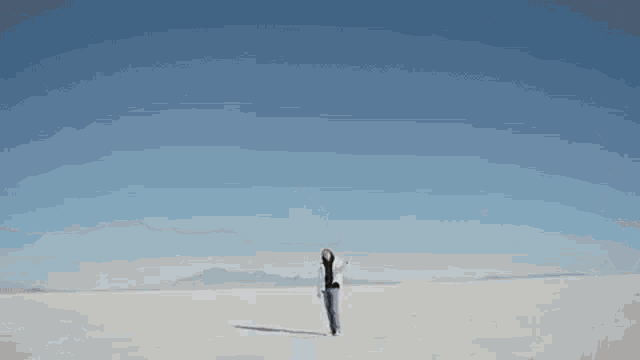 a woman wearing a white jacket and jeans is walking on a snowy field .