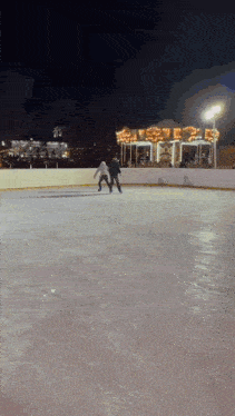 two people are ice skating in front of a carousel