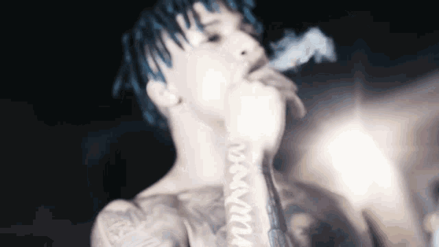 a man with blue hair is smoking a cigarette with a tattoo on his arm that says ' damn '
