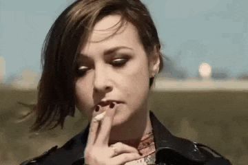 a woman in a leather jacket is smoking a cigarette in a field .