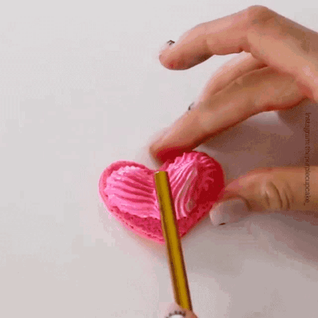 a person is frosting a heart shaped cupcake with a pencil .