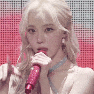 a woman with blonde hair is singing into a pink microphone on a stage .