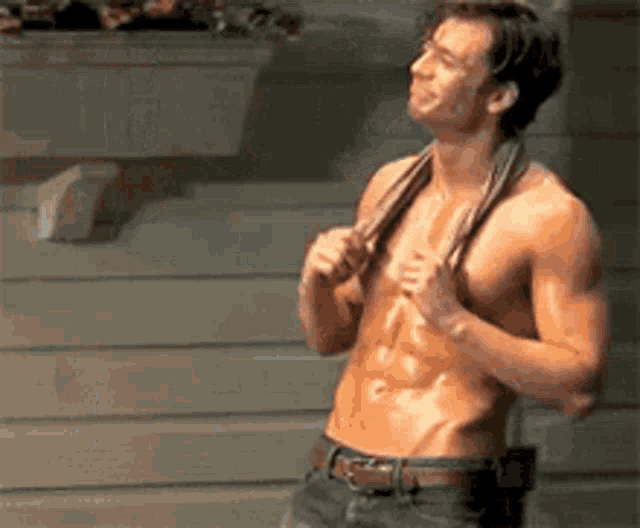 a shirtless man is holding a towel around his neck while standing in front of a wall .