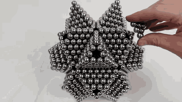 a hand is holding a piece of metal balls in front of a bunch of metal balls