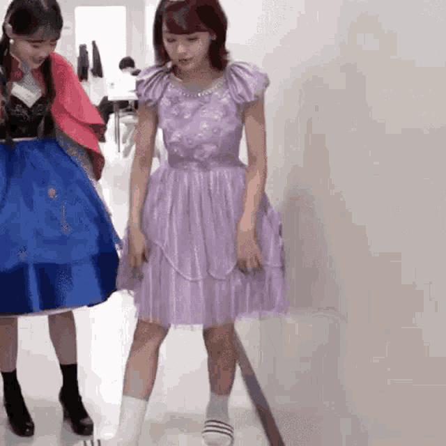 a girl in a purple dress is standing next to a girl in a blue dress .