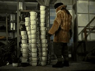 a man in a fur coat stands in front of a stack of cups