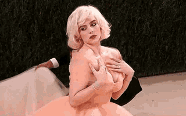 billie eilish is wearing a pink dress and holding her chest while standing next to a man .