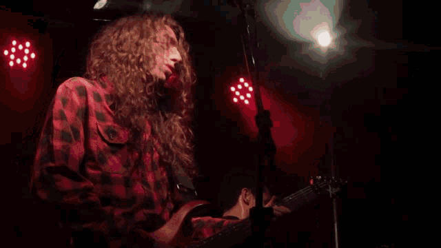 a man in a red plaid shirt is playing a guitar next to a drummer