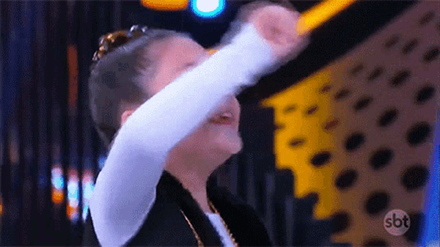 a young girl is dancing on a stage with her arms outstretched and a sbt logo in the background .