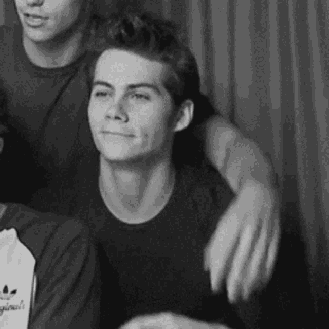 a black and white photo of a young man in a black shirt sitting next to another young man .