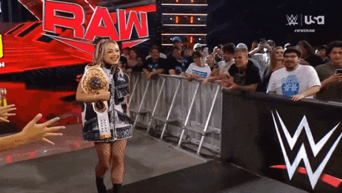 a woman is holding a wrestling championship belt in front of a raw logo