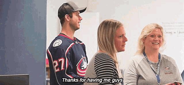 a man wearing a jersey with the number 27 on it is standing next to two women .