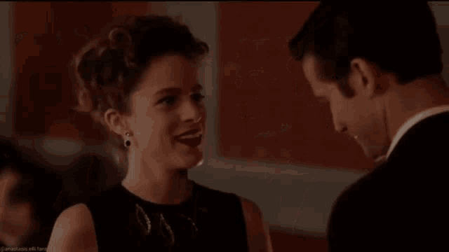 a man and a woman are looking at each other and smiling . the woman is wearing a black dress .
