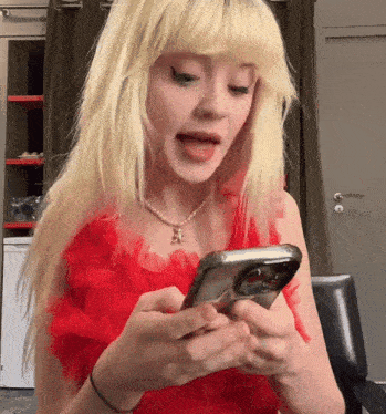 a blonde woman in a red dress is using a cell phone