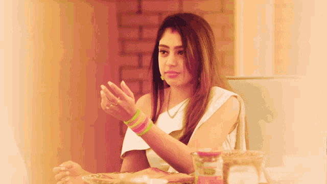 a woman in a white top sits at a table with a jar of sauce on it