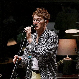 a man singing into a microphone wearing glasses and a plaid shirt