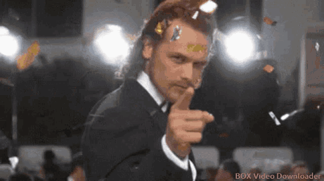 a man in a suit is pointing at the camera with a box video downloader logo in the corner