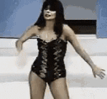 a woman in a black swimsuit is dancing on a stage in front of a white wall .