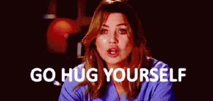 a woman in a scrub top is sitting in front of a blue background with the words `` go hug yourself '' .
