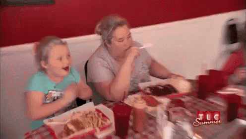 a woman and a little girl are sitting at a table eating a meal .