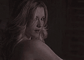 a naked woman is looking over her shoulder in a dark room .