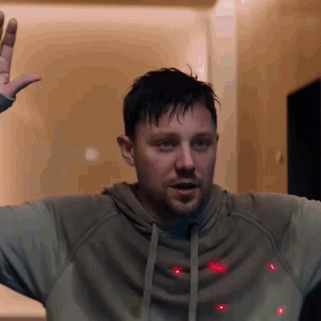 a man wearing a grey hoodie has red lights coming out of his chest
