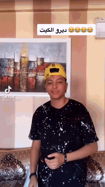 a young man wearing a black shirt and a yellow hat is standing in front of a painting on the wall