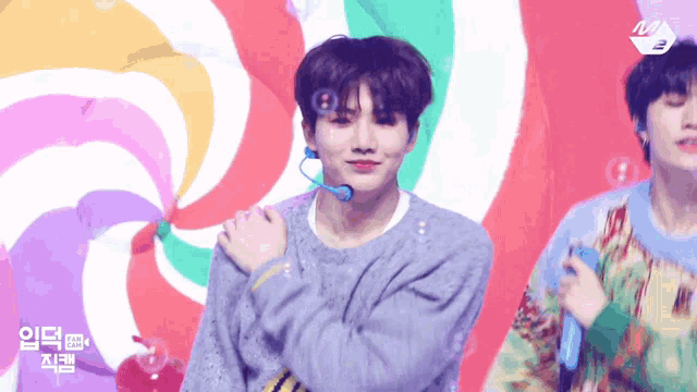 a man in a blue sweater is standing in front of a colorful swirl